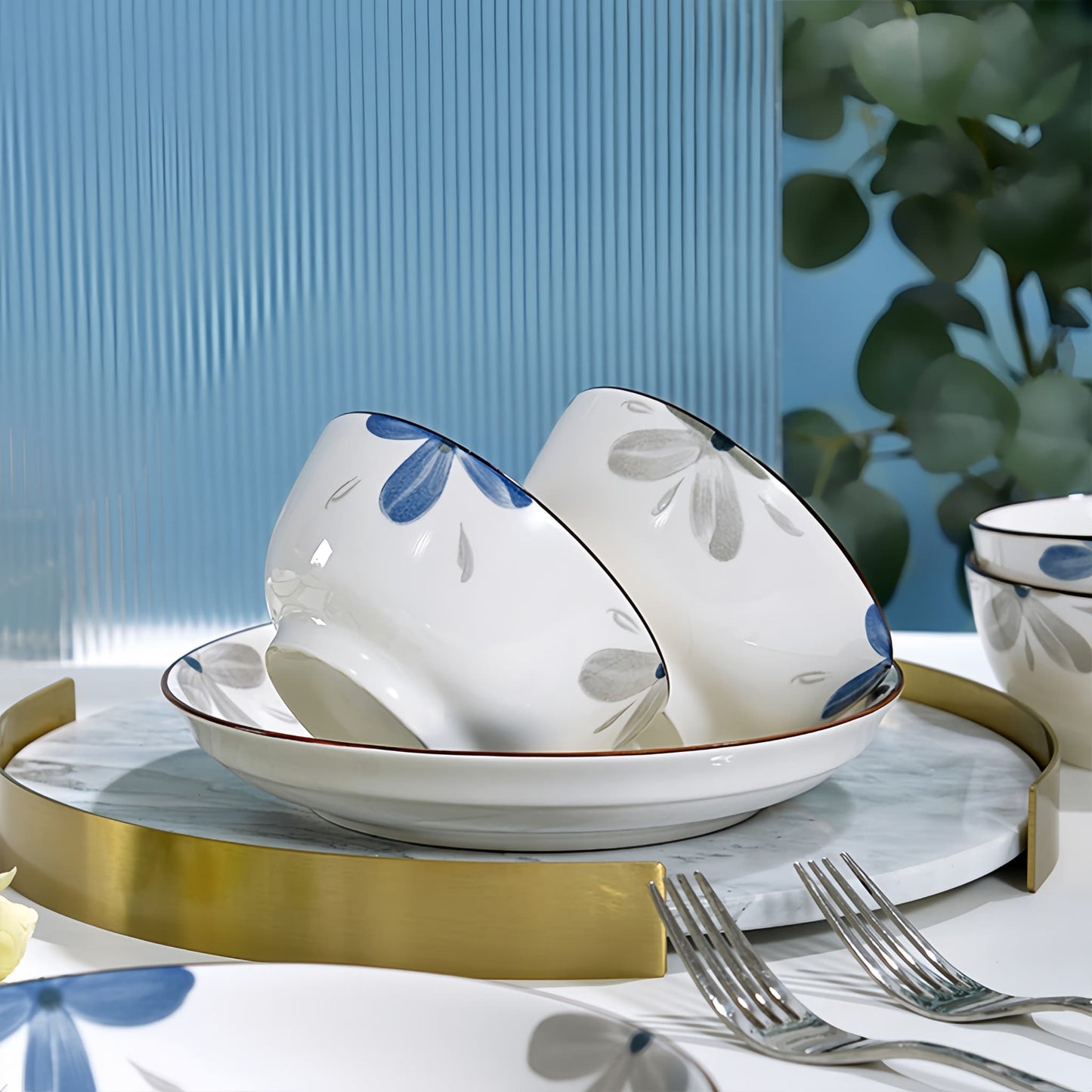 Ceramic bowls with floral patterns on a table setting with cutlery and a blue textured wall. YUNGPING Azure Future Everyday Ceramic Dinnerware Set, 10-Piece