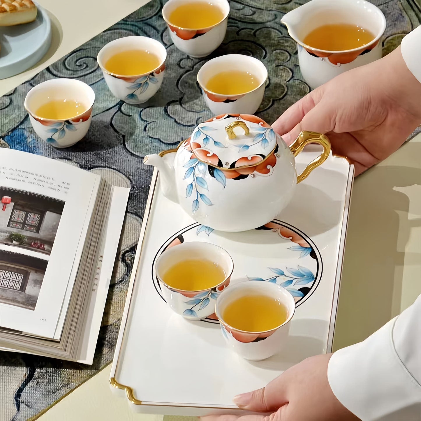 Tea service with a teapot and cups on a tray, with a hand holding the teapot lid. YUNGPING Autumn Garden Memory Fine Bone China Tea Set, Close-up detail