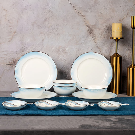 Dinnerware set with white plates and bowls on a gray surface with decorative elements. YUNGPING Azure Ivory Fine Bone China Dinnerware Set, 16-Piece, styled on an elegant dining table for formal hosting and special occasions.