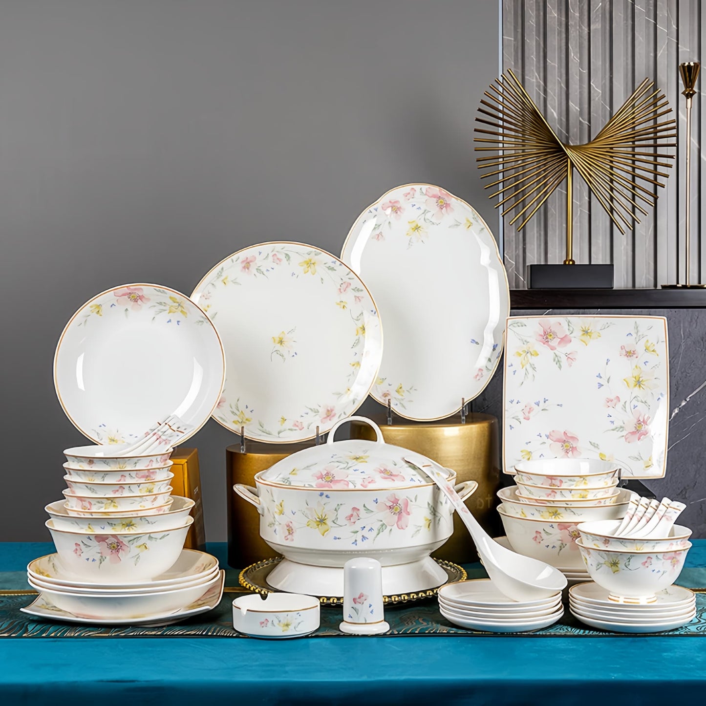 Set of floral-patterned dinnerware on a blue surface with decorative elements in the background. YUNGPING Spring Bloom Breeze Fine Bone China Dinnerware Set, 50-Piece, styled on an elegant dining table for formal hosting and special occasions.
